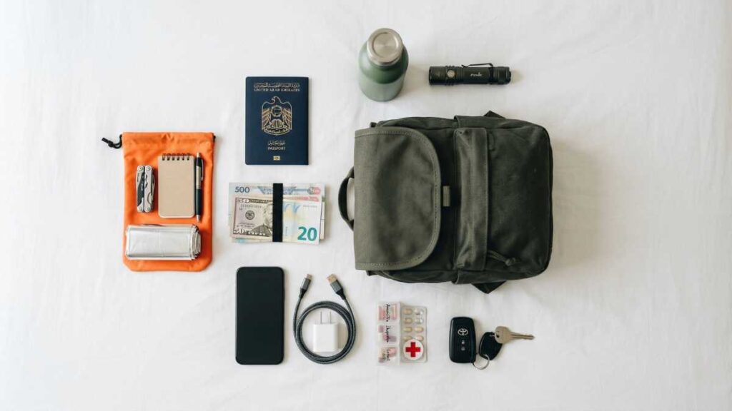 Overhead view of emergency travel essentials neatly arranged on white surface including passport cash phone charger medications and car keys